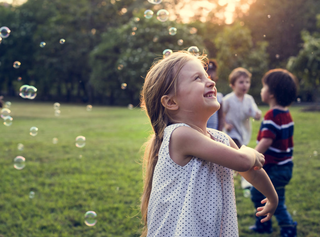 Girl smiling as bubbles fall aorund her with the sunsetting and other kids in the background.