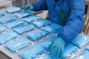 Blue paper facemasks being prepared for distribution by someone in sterile gear