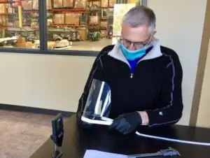 Older man in facemask handling a face shield.
