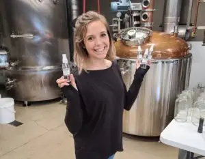 Woman holding bottles of hand sanitzer smiling in Cultivated Cocktails distillery room
