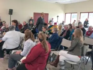Many people in large room with chairs and man walking around.
