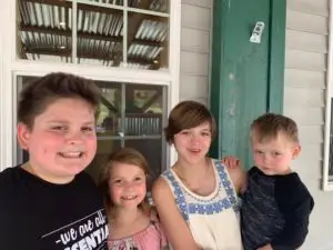 4 siblings standing on their porch smiling.