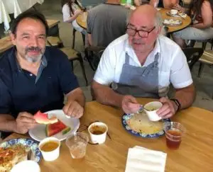Two men enjoying watermelon and chili at a restaurant table