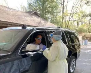 Healthcare worker in head to toe protective gear speaking with driver in car.