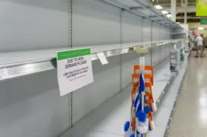 Close up empty toilet paper shelves with sign warning about purchase limit
