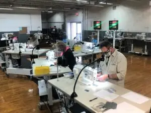 People wearing masks in a large room working at sewing machines to make face masks