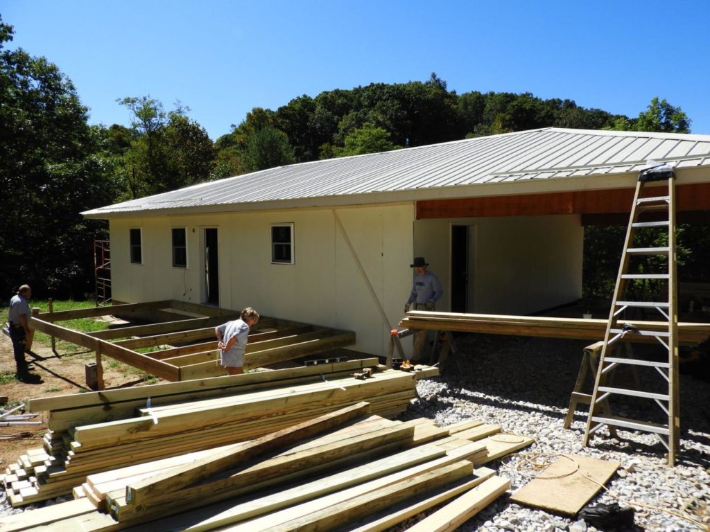 Single story home in the midst of being build with 3 volunteers helping.