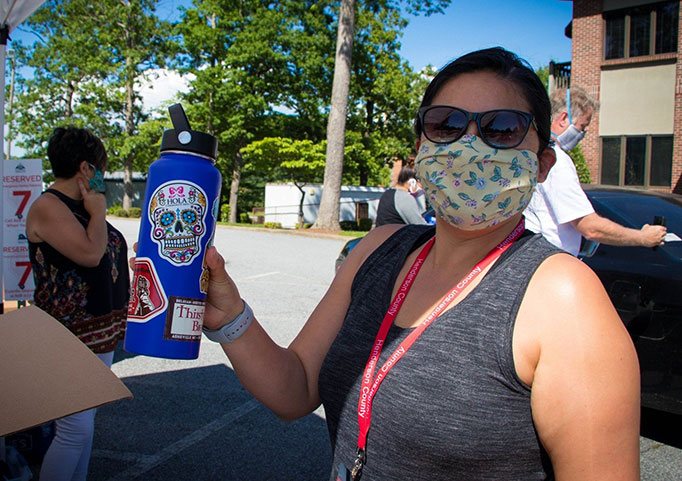 Woman in mask and sunglasses holds up water bottle with a candy skull sticker.