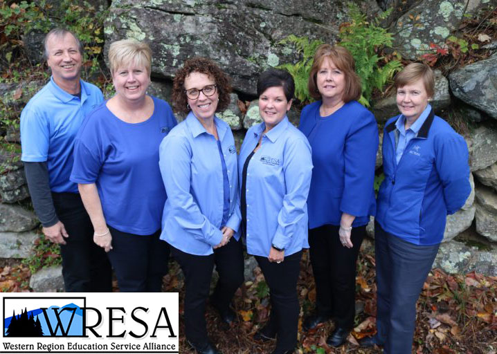 The WRESA staff standing in front a rock outside all wearing shades of blue.
