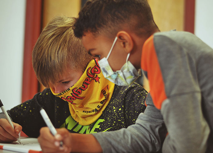 2 young boys wearing facemasks doing homework together