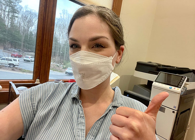 Woman wearing mask inside office with a thumbs up.