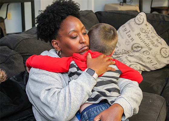 Woman embraces toddler while sitting on a couch