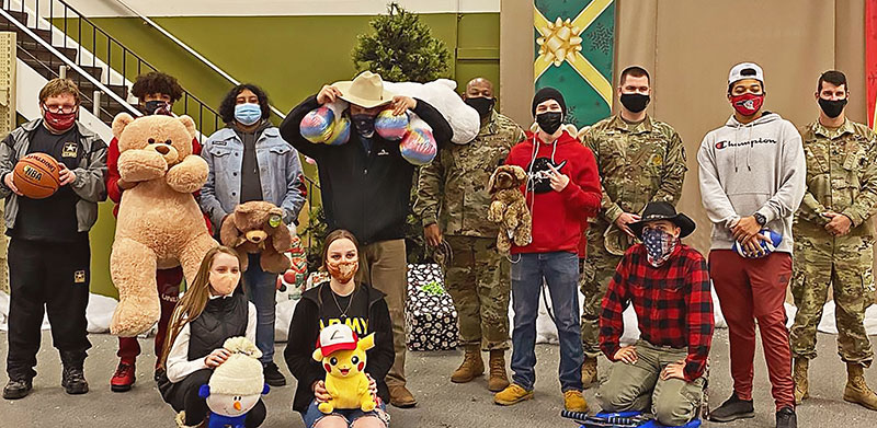 Group of children, people in costumes, and military personnel standing together with stuffed animals.