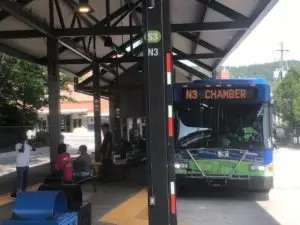 Outdoor bus stop with blue and green bus with "N3 Chamber" on sign