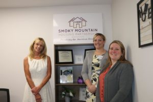 3 women standing in front of an award shelf for the Smoky Mountain Housing Partnership