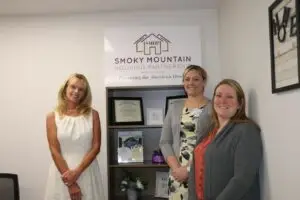 3 women standing in front of an award shelf for the Smoky Mountain Housing Partnership