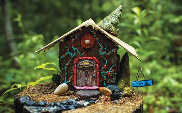 Handmade mini fairy house with "believe" sign in the woods