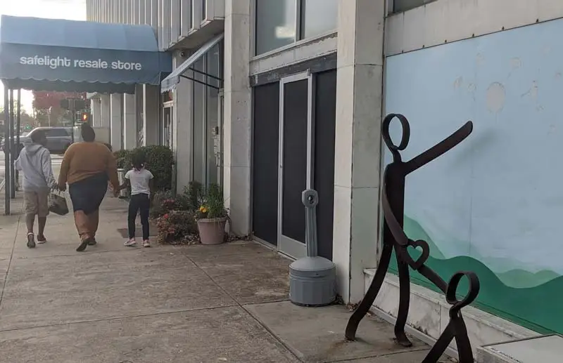 Mom and two children walk towards store entrance with iron sculpture in the foreground.