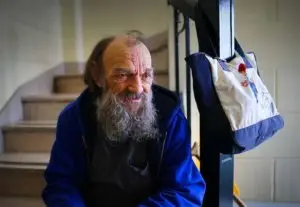 Elderly man sitting on a staircase with his bag hanging on the riail next to him.