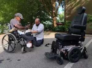Man helping amputee in old wheelchair get ready for a new electric wheelchair.