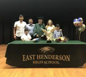 Family stand behind a table with a green table cloth, baloons, flowers, and a eagle statue.