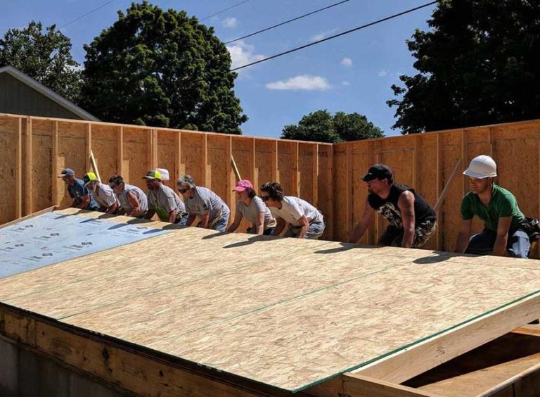 Group of volunteers lifting up the frame of a wall for a house.