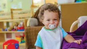 Toddler with a pacifer in their mouth standing in a play room