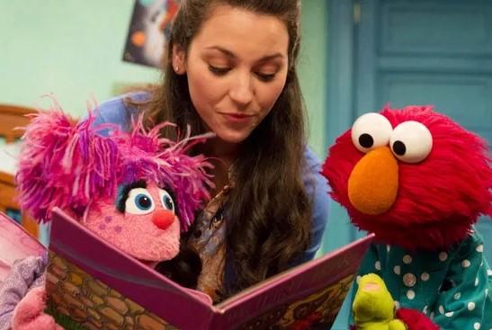 Woman reading with Elmo and another Sesame Street character