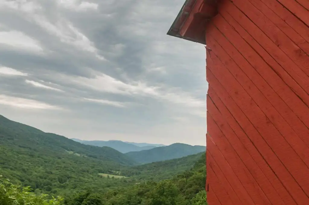 side of red barn with forested mountains in background