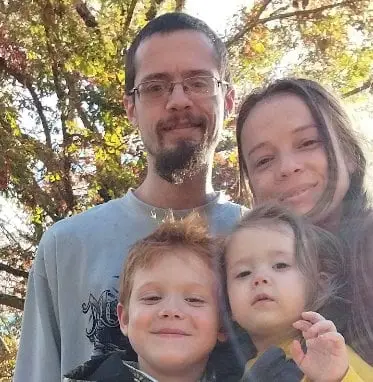 family of four smiling for selfie photo with tree in background
