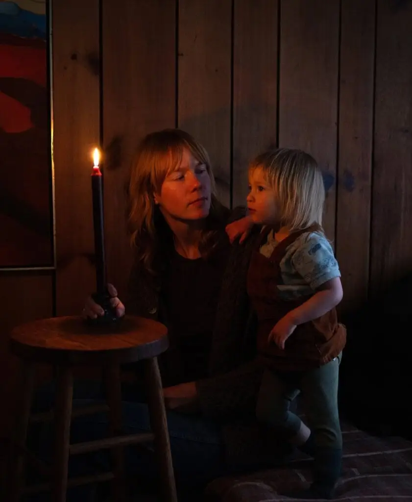 mother holding child next to lit candle in dark room