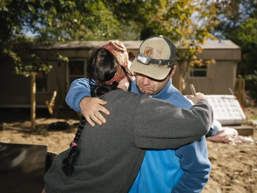 man and woman hugging in front of damaged home after Hurricane Helene